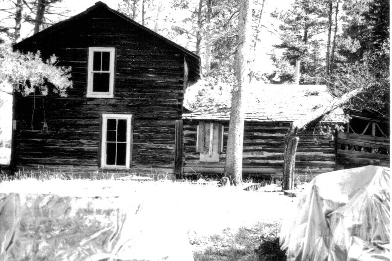 Antique photo of two story cabin surrounded by large evergreens.