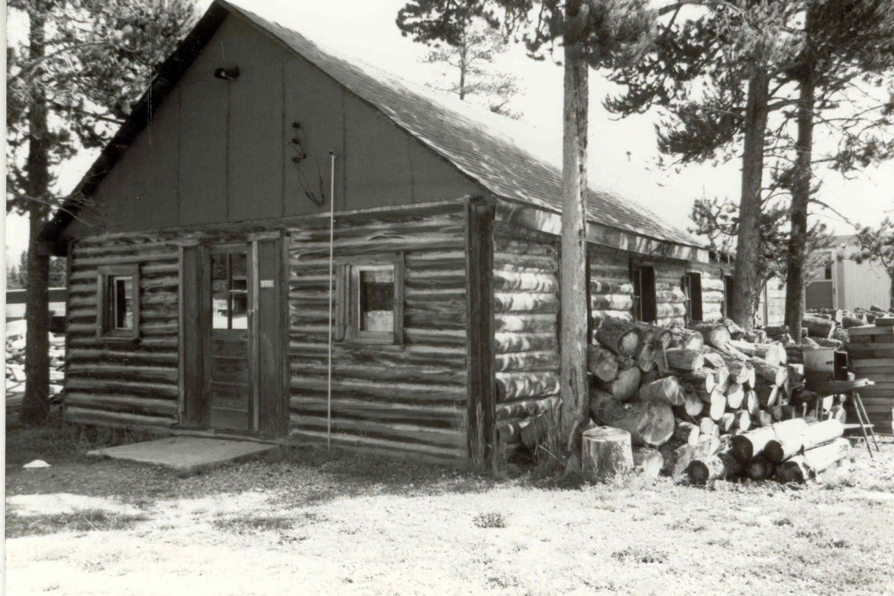 Black and white photo of the Log Chapel and woodpile, taken at its original location
