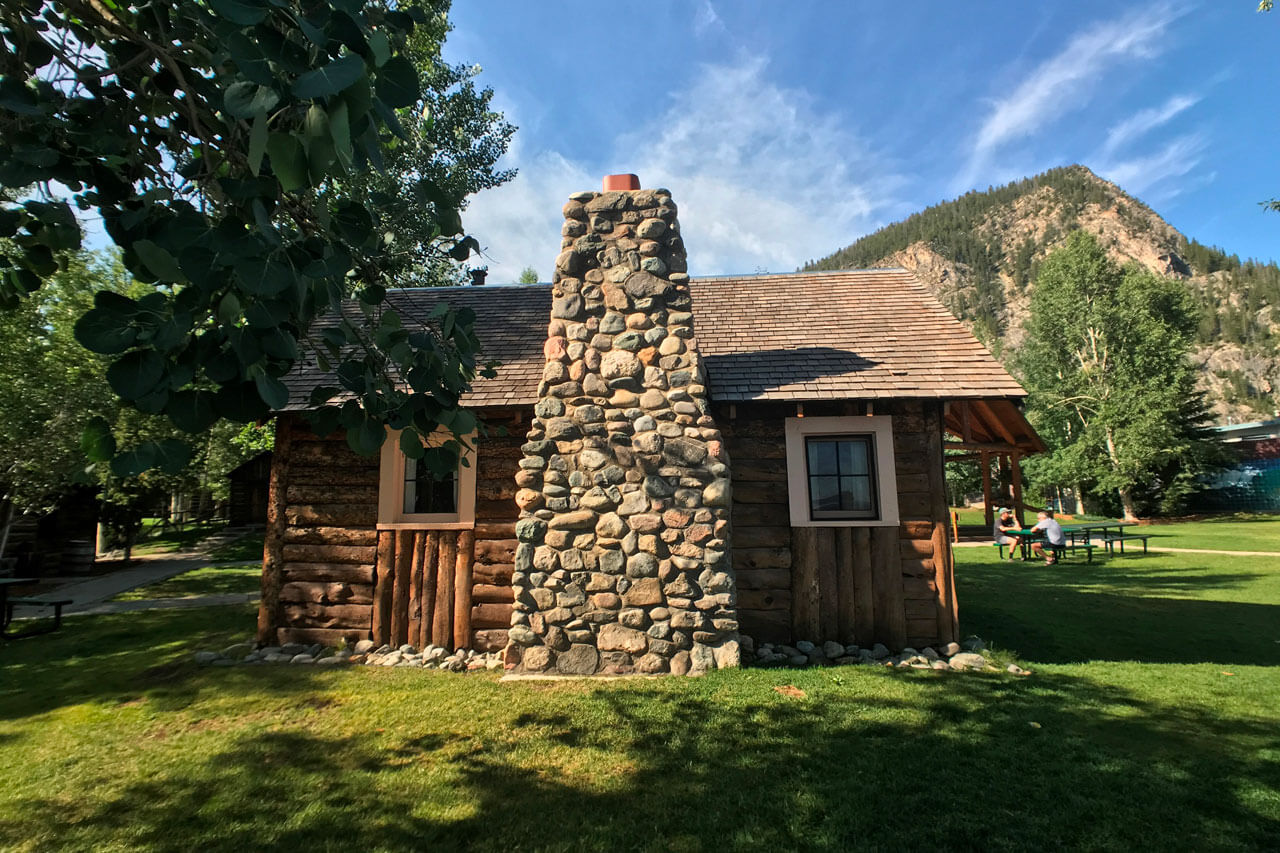 Log cabin with large stone chimney and tree covered mountains in background