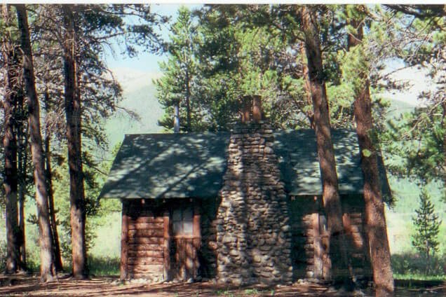Small cabin in the dappled light shining through the large pines that surround it.