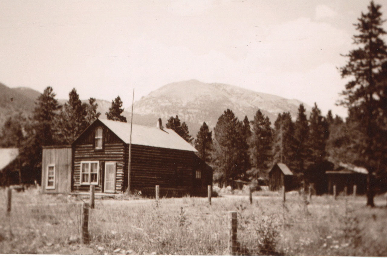 Antique black and white photo of cabin with mountains in background