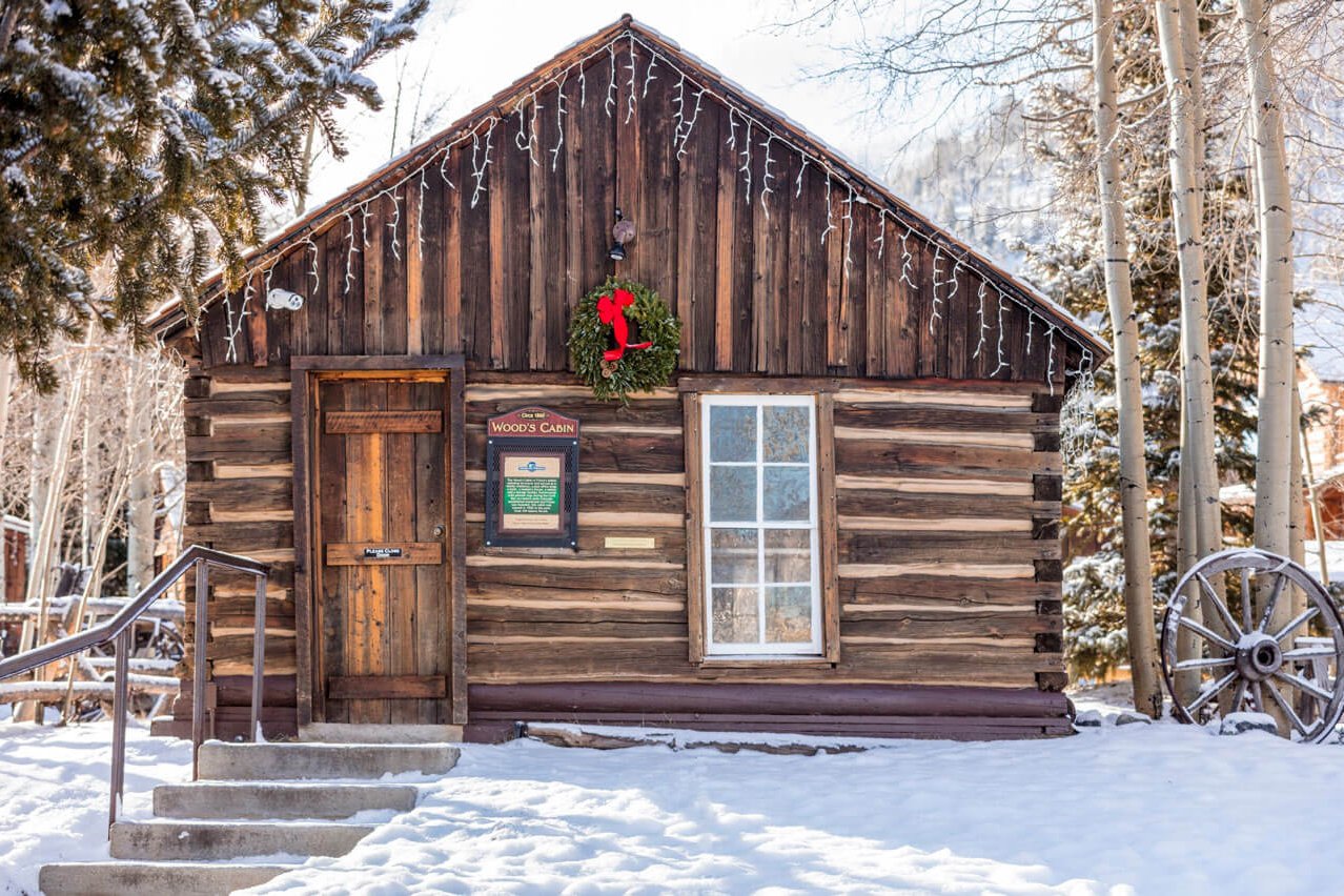 Log cabin with Christmas wreath surrounded by snow on a bright, sunny day