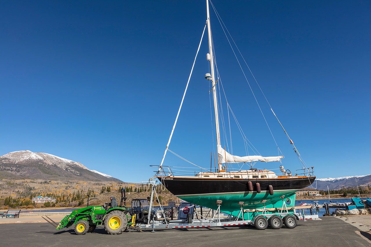 Large black and teal sailboat on a trailer hauled by green tractor.