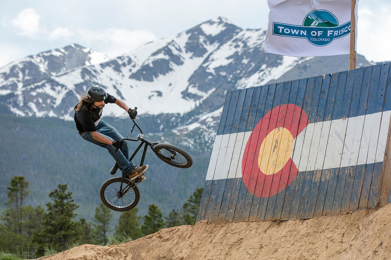 Man on bike hitting wall feature with mountains in background at Frisco Bike Park