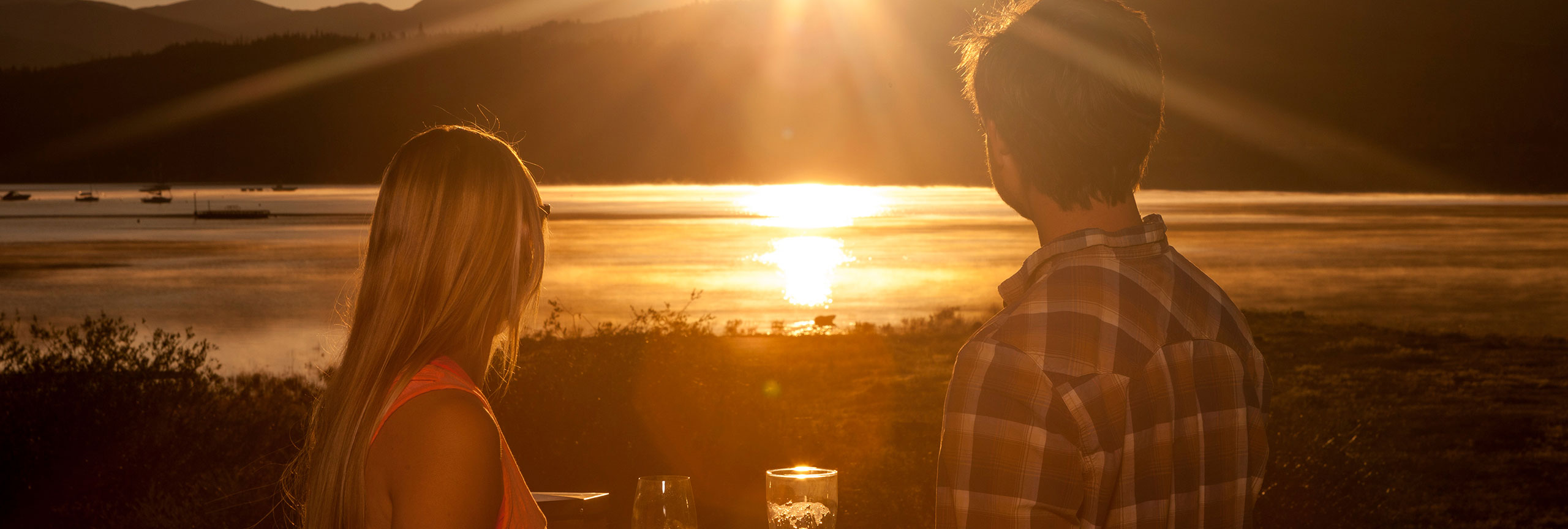 Couple enjoying drinks on a deck overlooking Lake Dillon at sunset.