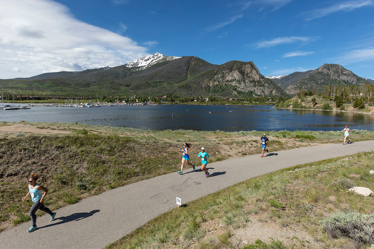 Runners running on rec path with Dillon Reservoir and Ten Mile mountains in background