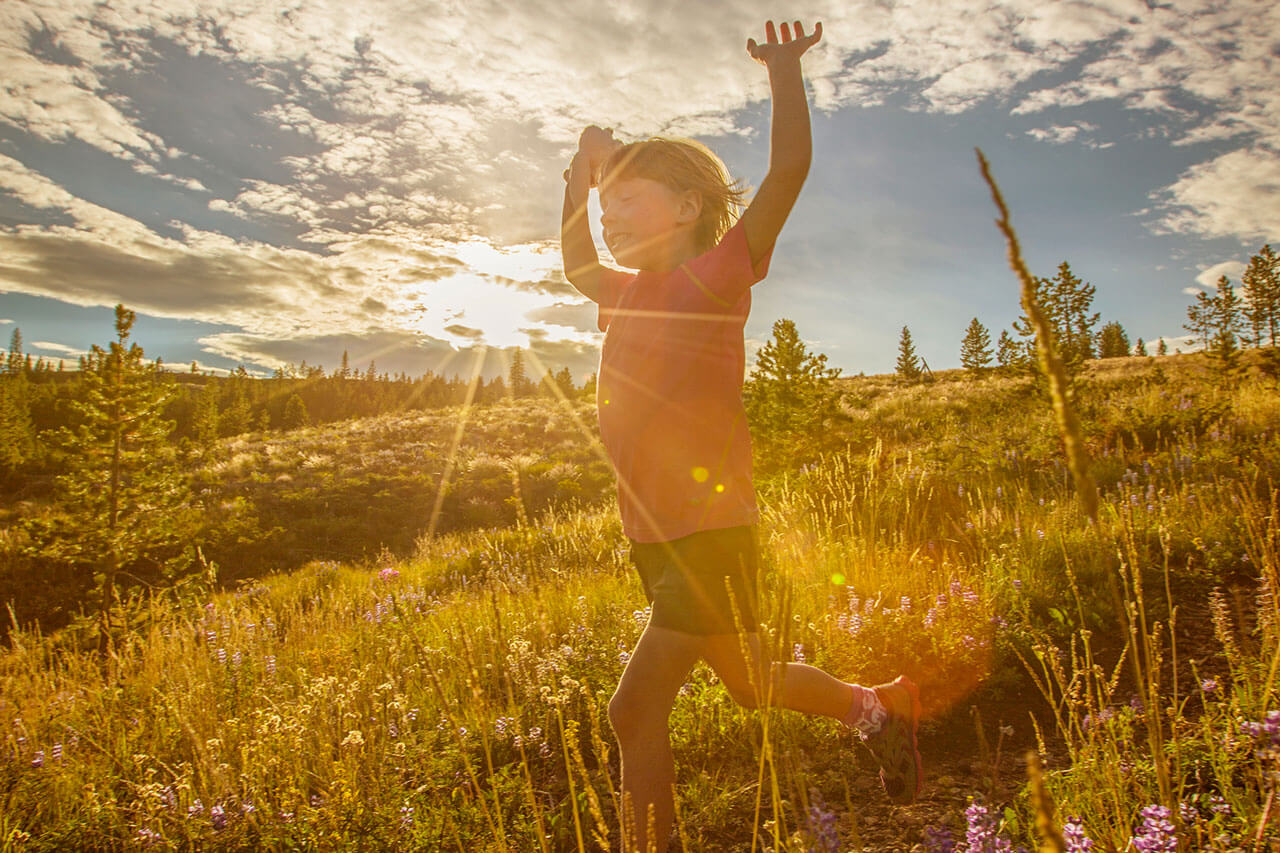 Happy little girl running on trail with hands up.