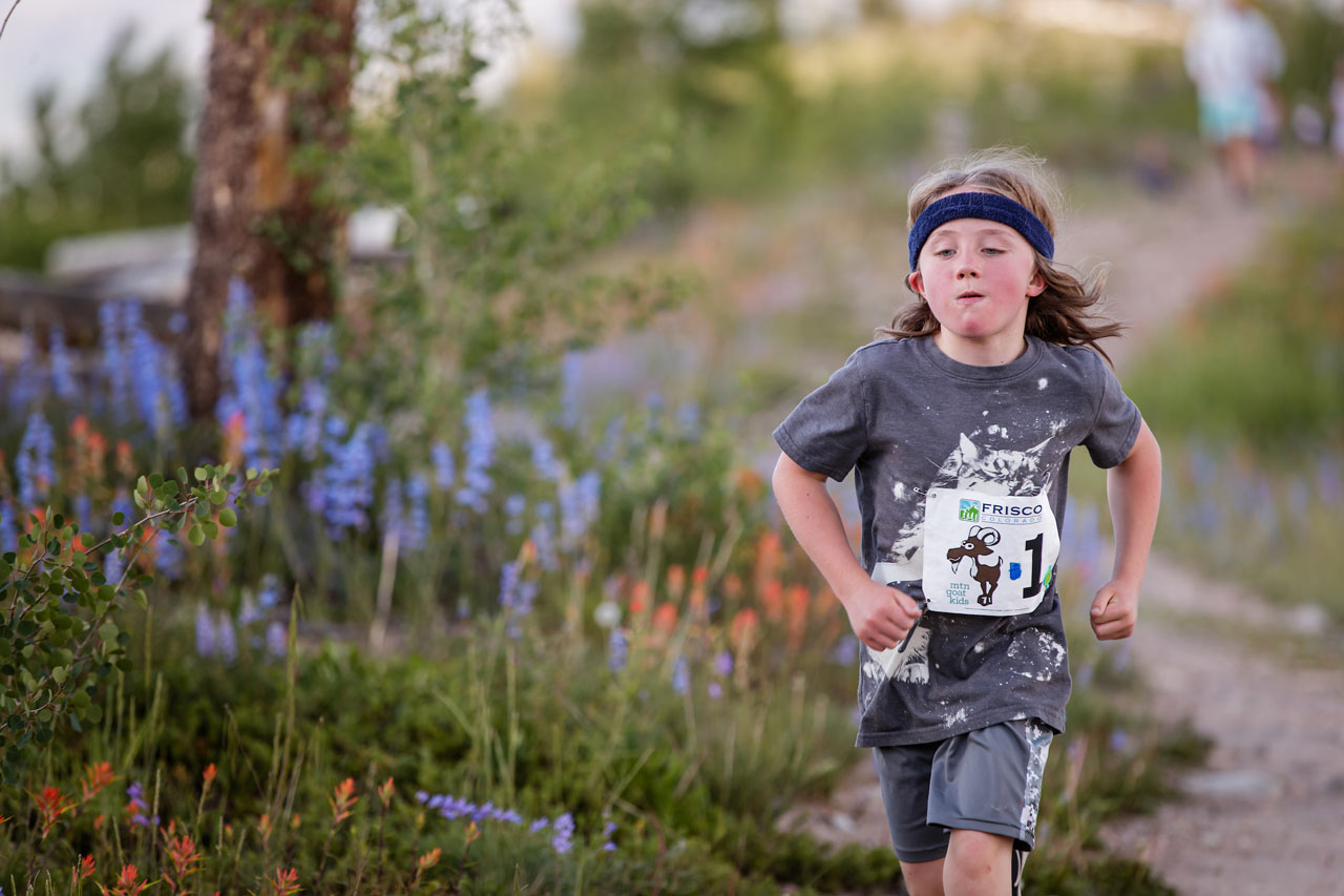 A young boy wearing a headband running on a trail with wildflowers.