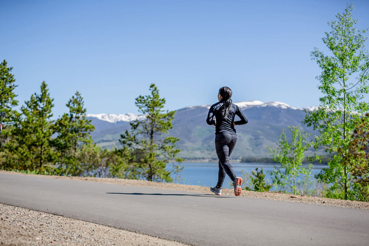 A runner on the rec path with lake and mountains in the background.