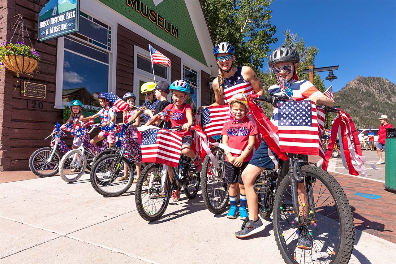 Group of kids and woman on bikes decorated with American flags at 4th of July parade
