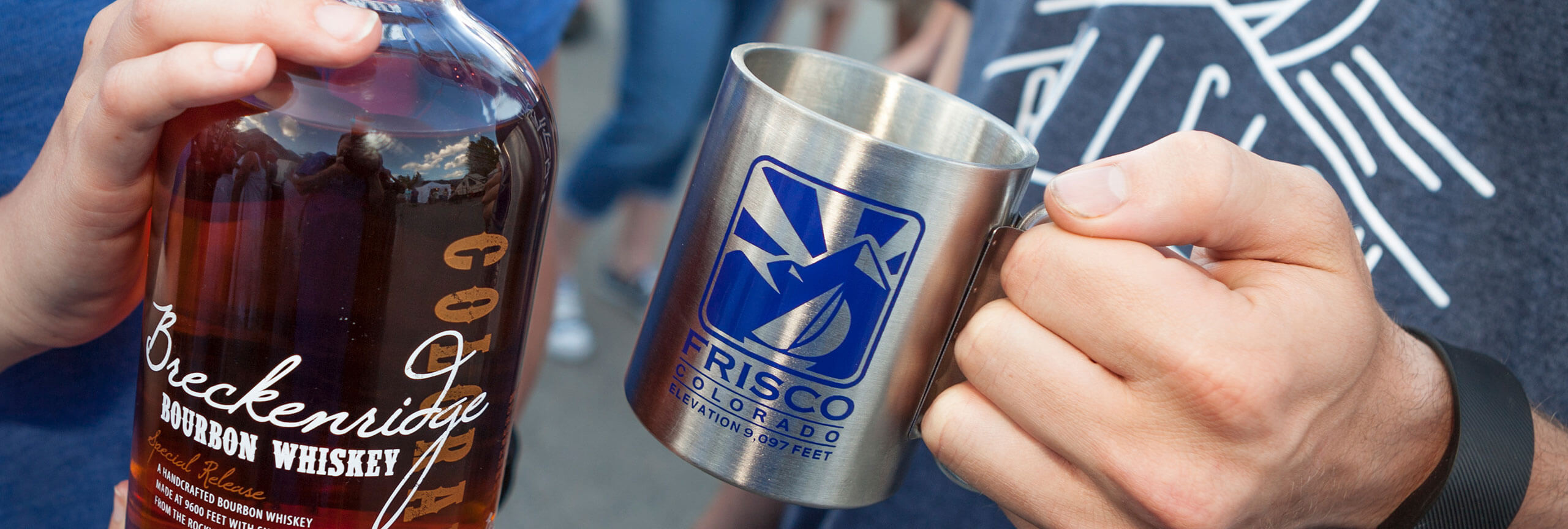 Close-up of stainless steel mug with Frisco logo and a bottle of whiskey from the Breckenridge Distillery.