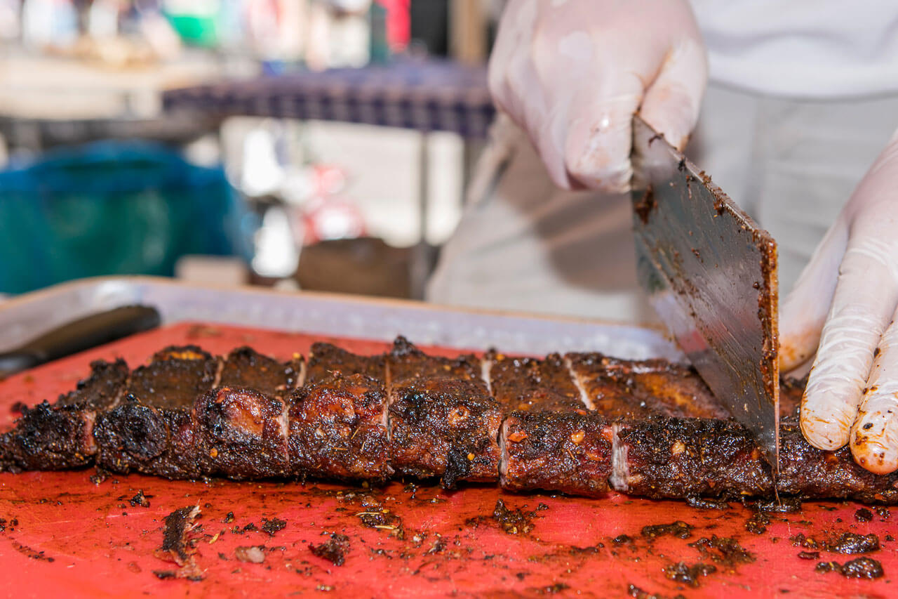Close-up of BBQ ribs being chopped on a red cutting board.