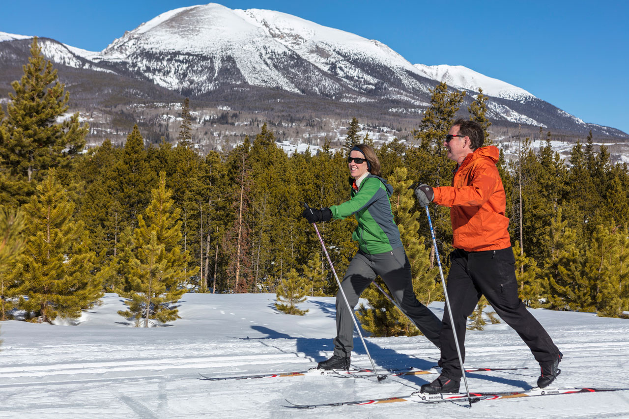 A man and woman cross country skiing on sunny day with Buffalo Mountain in the background.