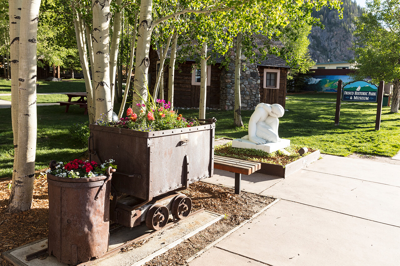 Old mining carts filled with colorful flowers and a white sculpture at Historic Parkat