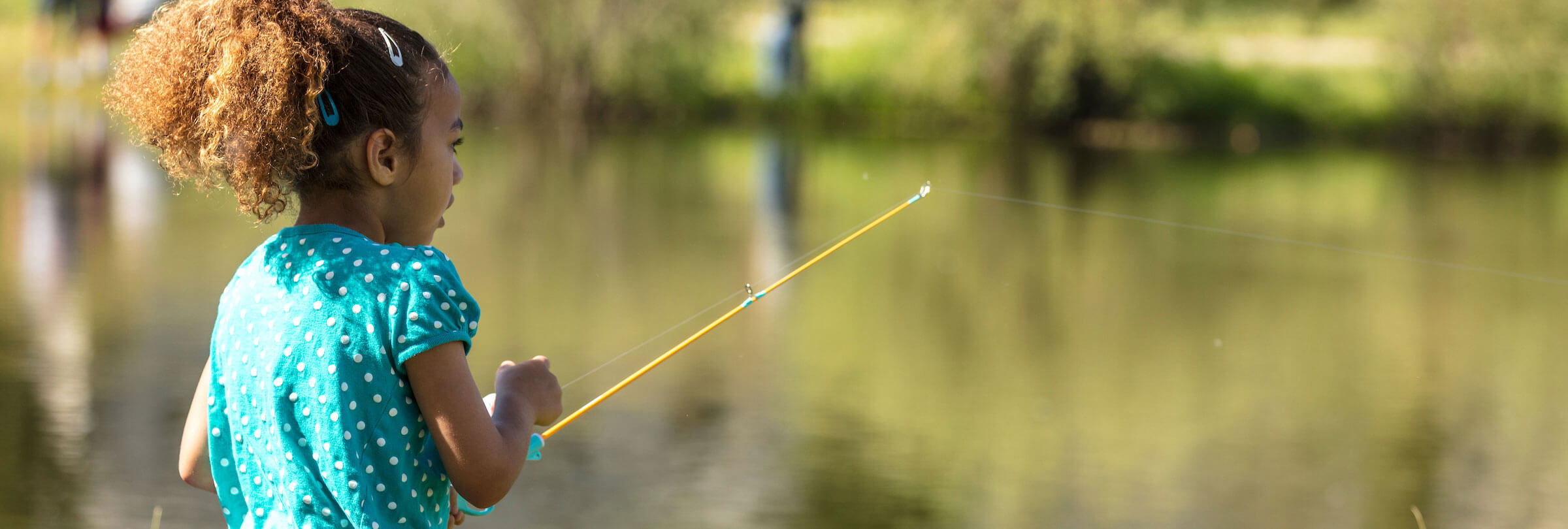 Close up of young girl in blue dress fishing at a pond.