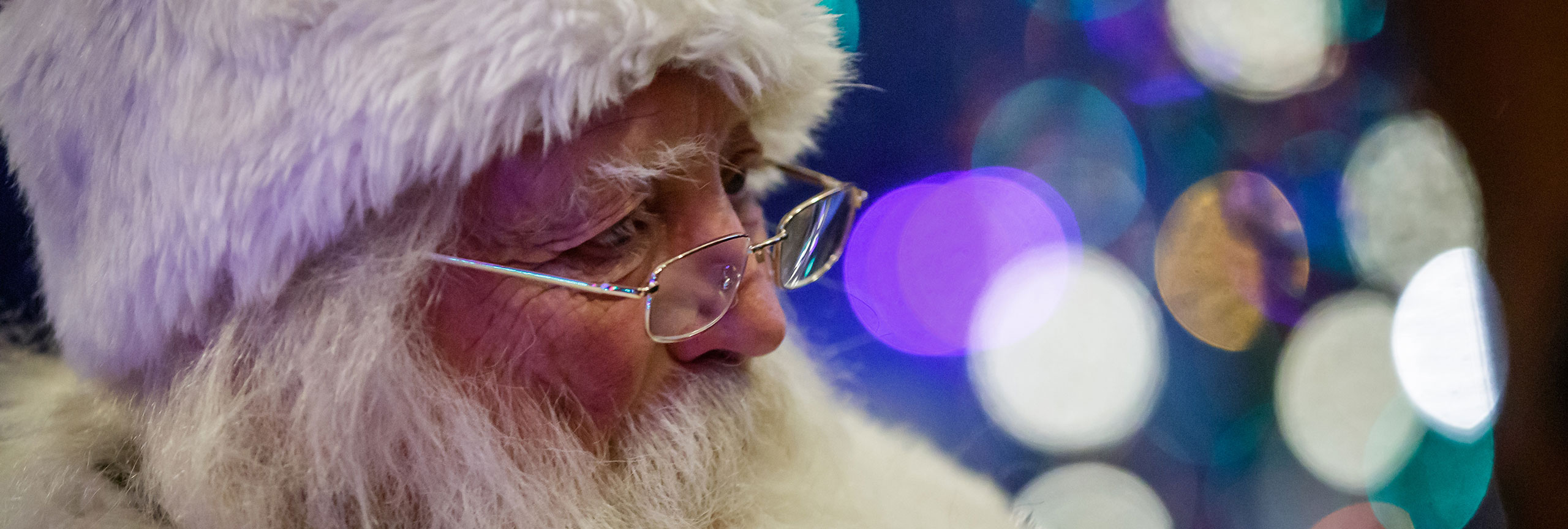 Closeup of Santa Clause with holiday lights in the background.