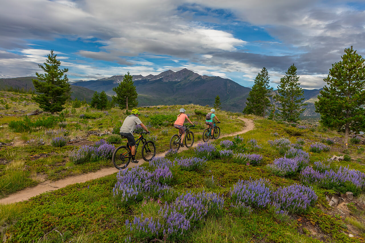 Three mountain bikers on a trail with Tenmile Range in the background.