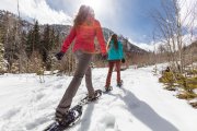 Two women snowshoeing in a trail on a sunny winter day.