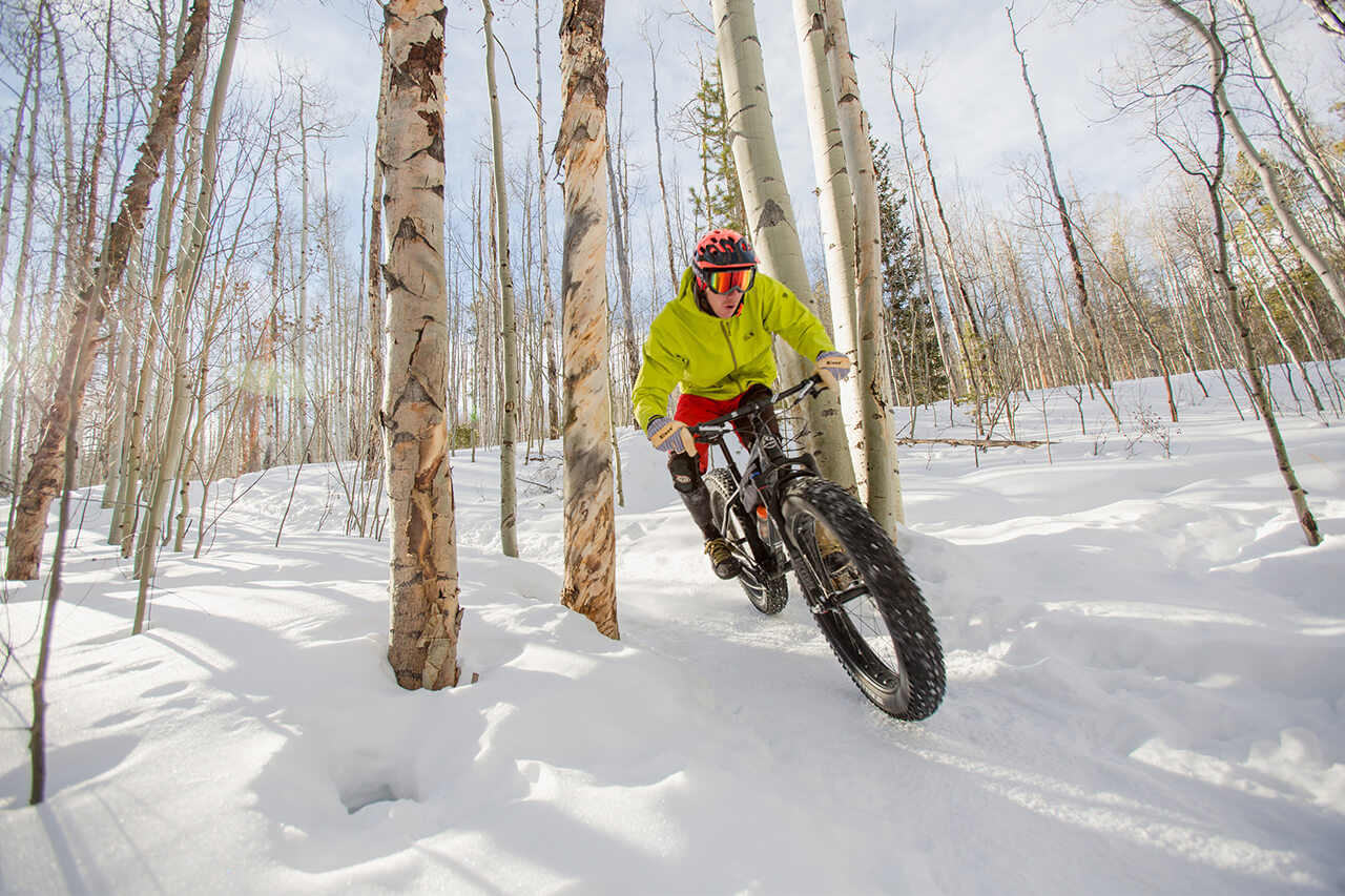 A rider on a fat-tire bike on a snowy, groomed trail in the trees.