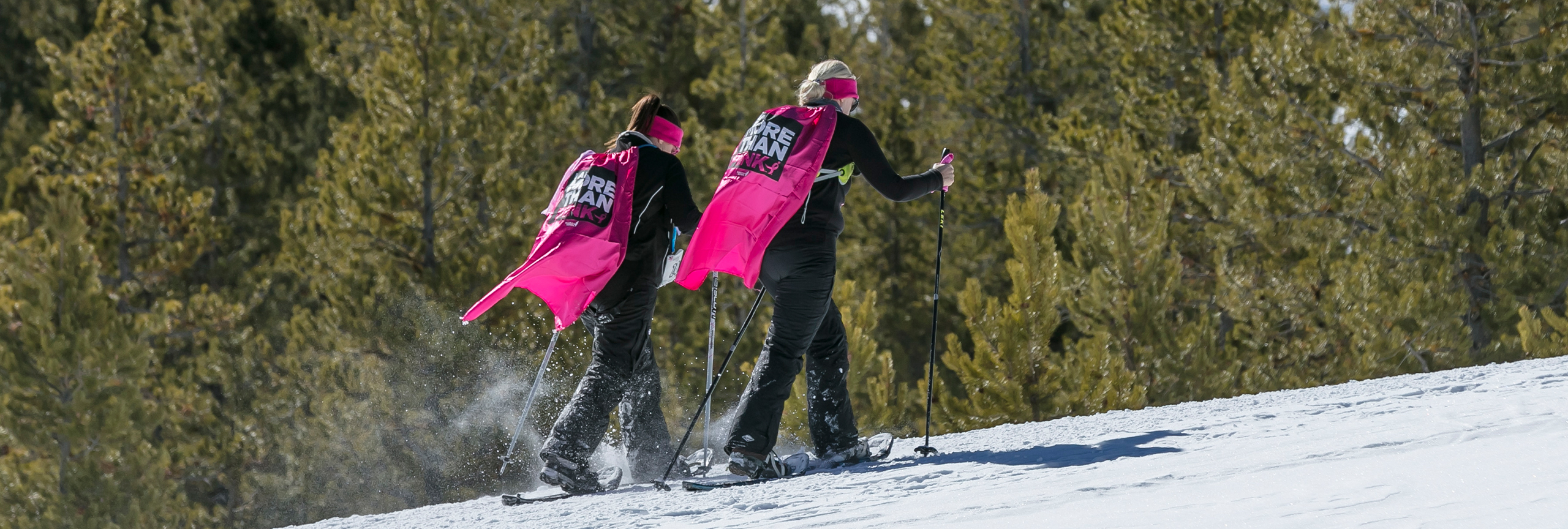 Two women dressed in pink, snowshoeing.