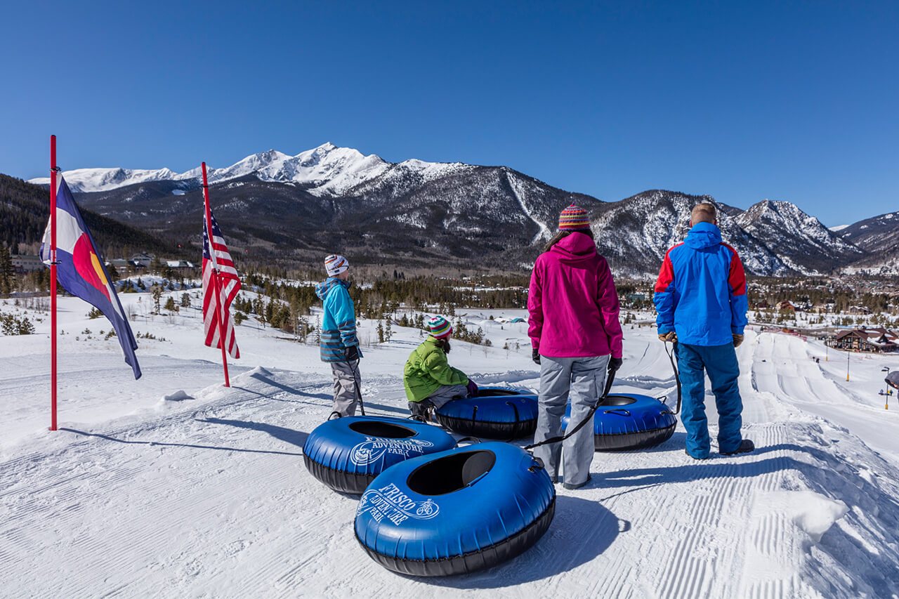 Man, woman , and two kids standing at top of tubing hill looking at mountain views
