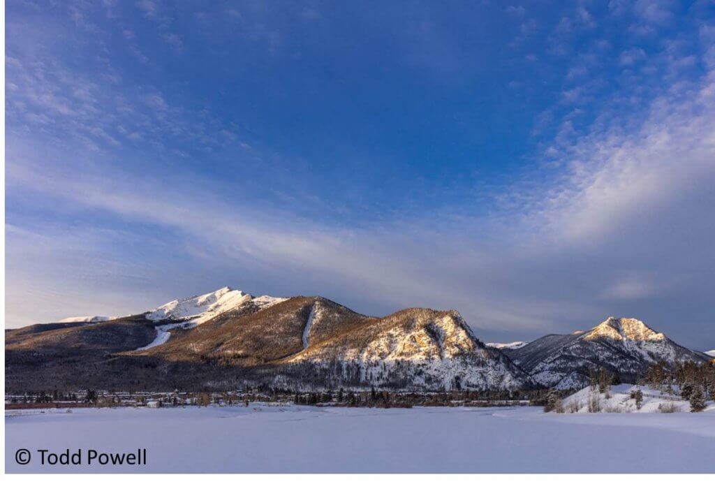 The sun illuminates the mountains and fresh snow across frozen Dillon reservoir