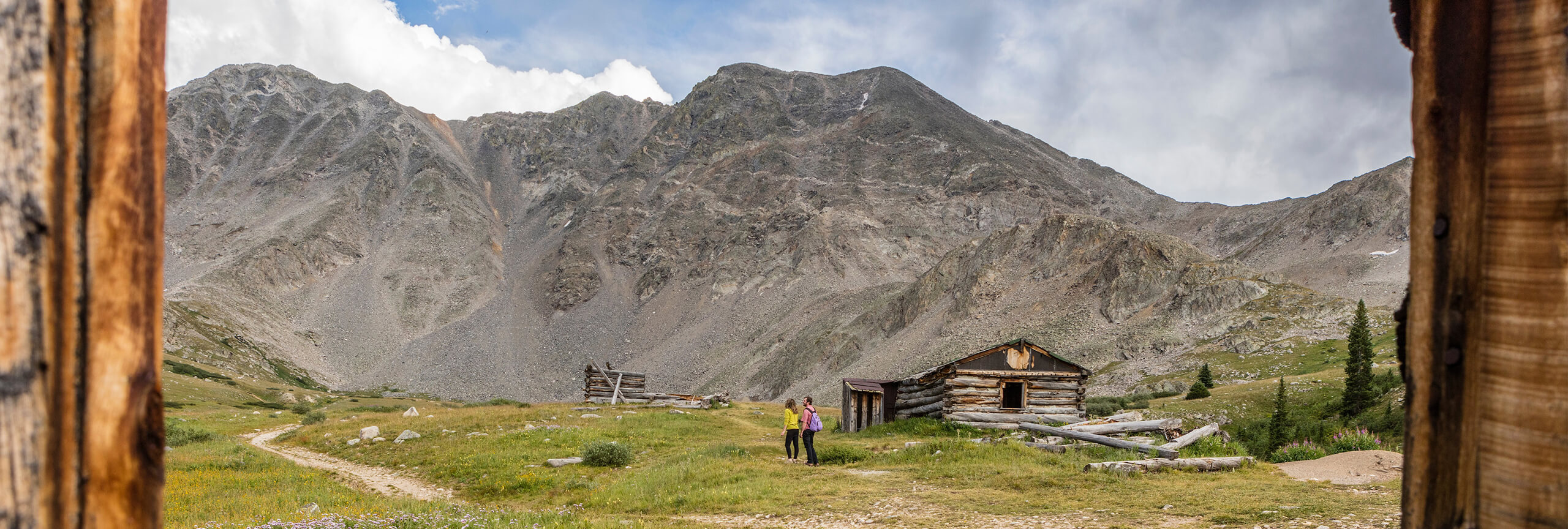 Man and woman hiking on trail near old building at Mayflower Gulch
