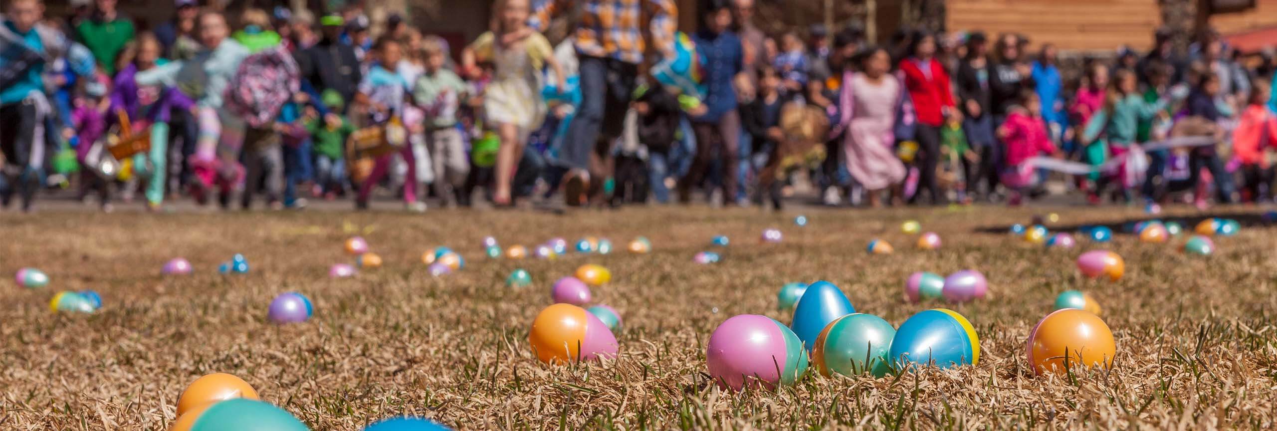 Easter Eggs on grass and kids running at Easter Egg Hunt