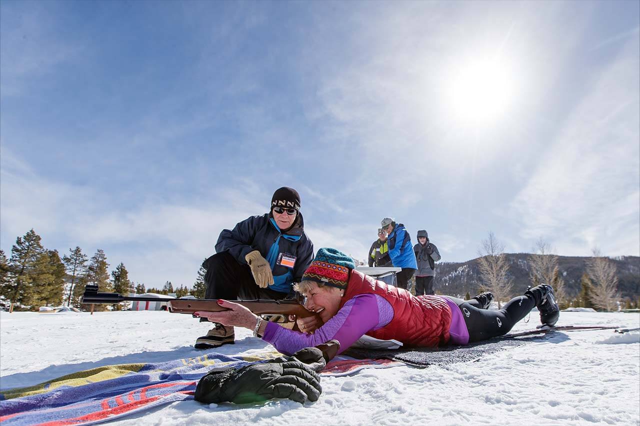 Woman on the ground with skis on shooting during a biathlon at the Frisco Nordic Center