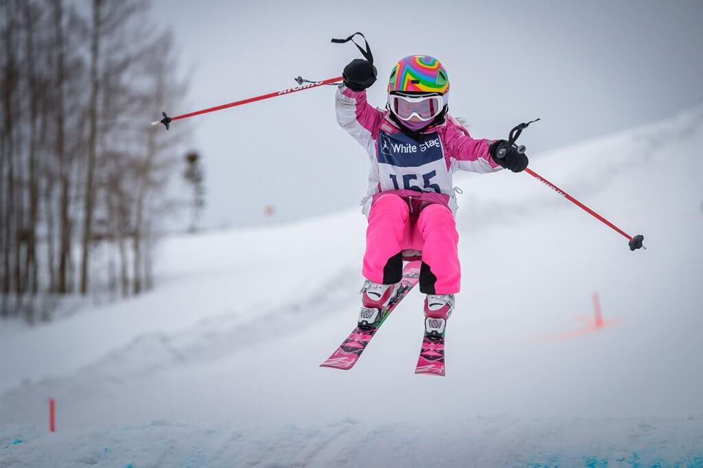 Girl in pink outfit getting air on skis at beginner ski/ride hill at Frisco Adventure Park
