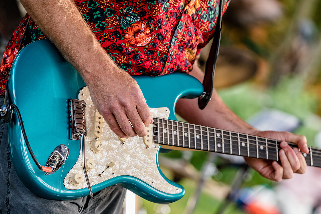 Close up of man in red shirt playing teal guitar